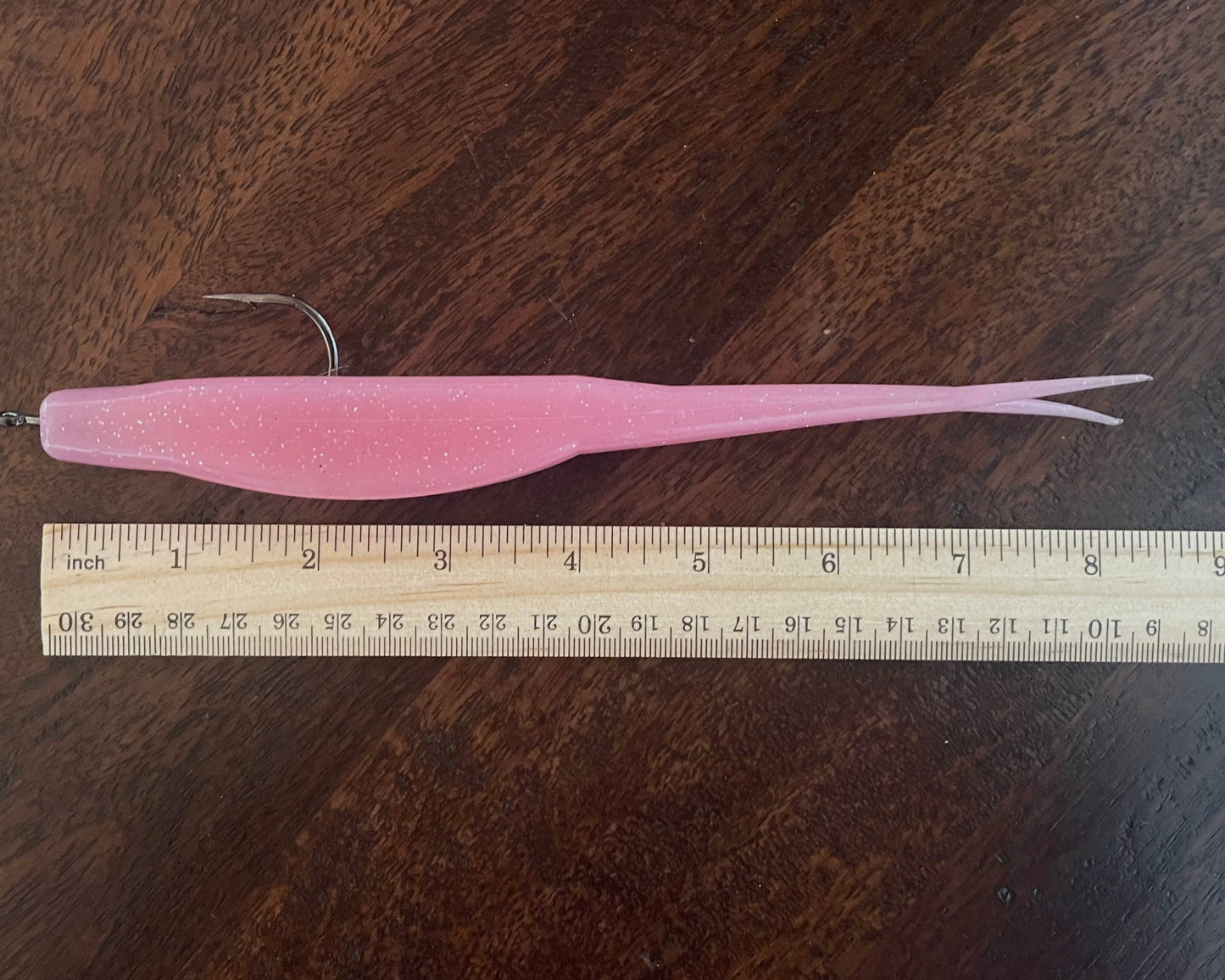 Pink fishing lure next to a ruler on a wooden surface
